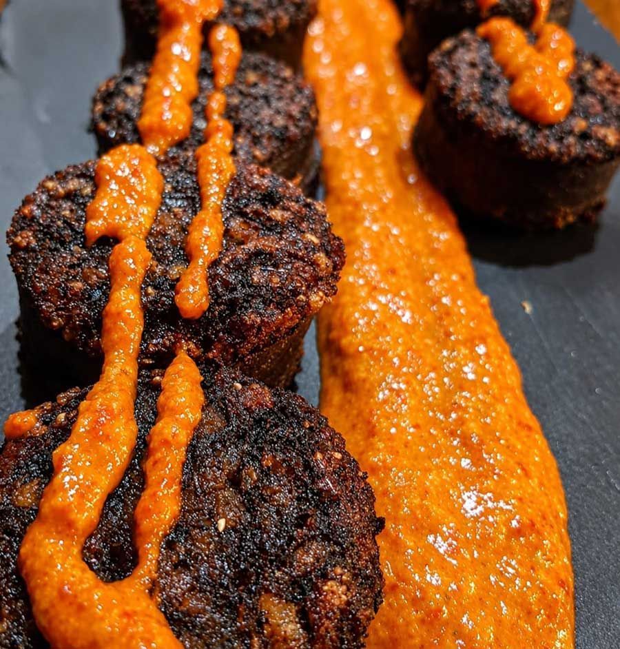 Bolas de comida fritas negras cubiertas con salsa de naranja en un plato oscuro.