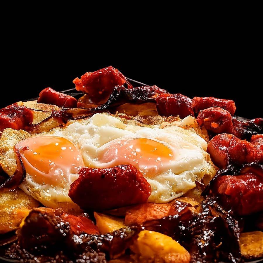 Huevos fritos cubiertos con tocino crujiente sobre un plato tostado para el desayuno sobre un fondo negro.