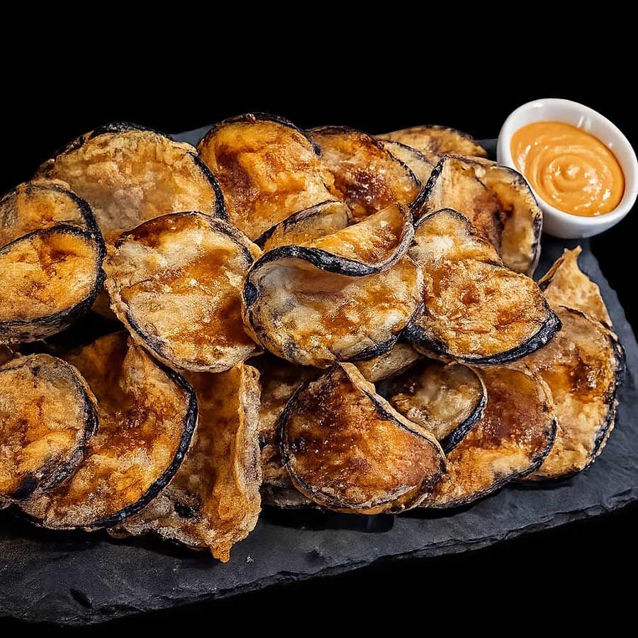 Rodajas de berenjena fritas y crujientes en un plato de pizarra negra con una pequeña taza de salsa para mojar.