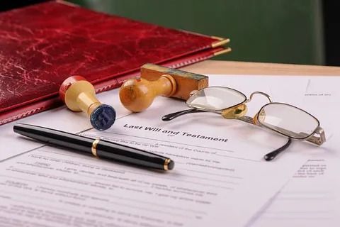 Documentos legales, bolígrafo, sellos, gafas y un libro rojo sobre una superficie de madera.