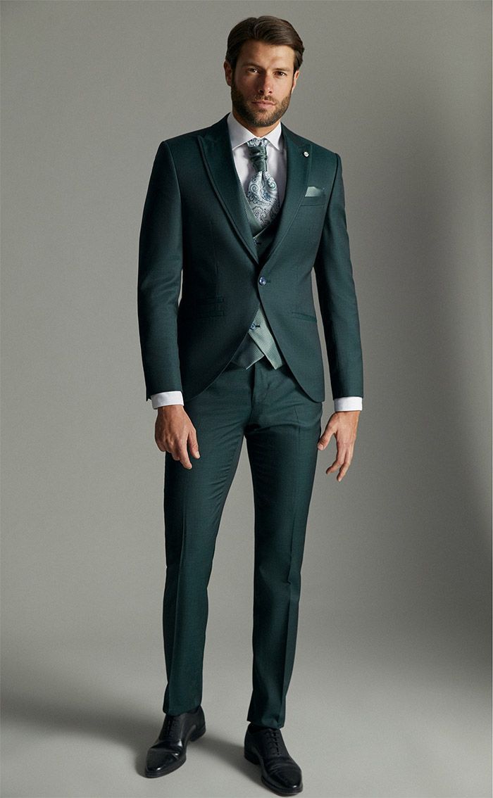 Home amb vestit i corbata de color verd blavós davant d’un fons gris llis