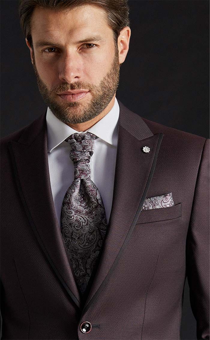 Home amb un vestit de color bordeus fosc, corbata estampada i mocador de butxaca, sobre un fons fosc