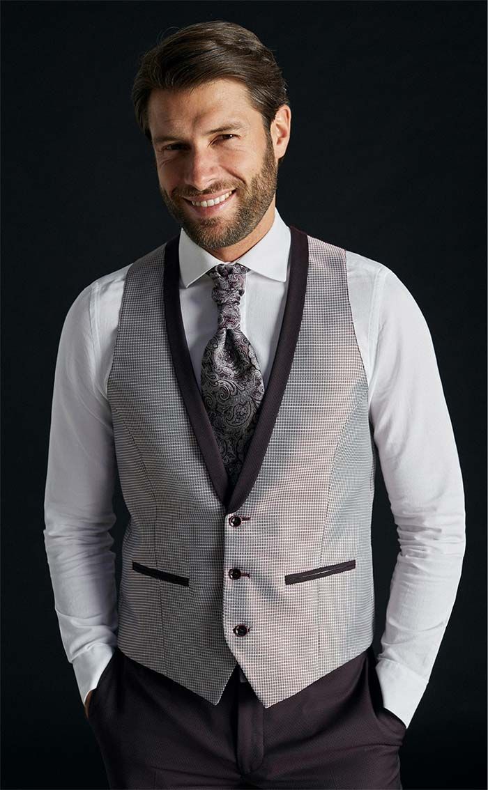 Home somrient amb camisa blanca, armilla de ratlles grises i corbata sobre un fons fosc.