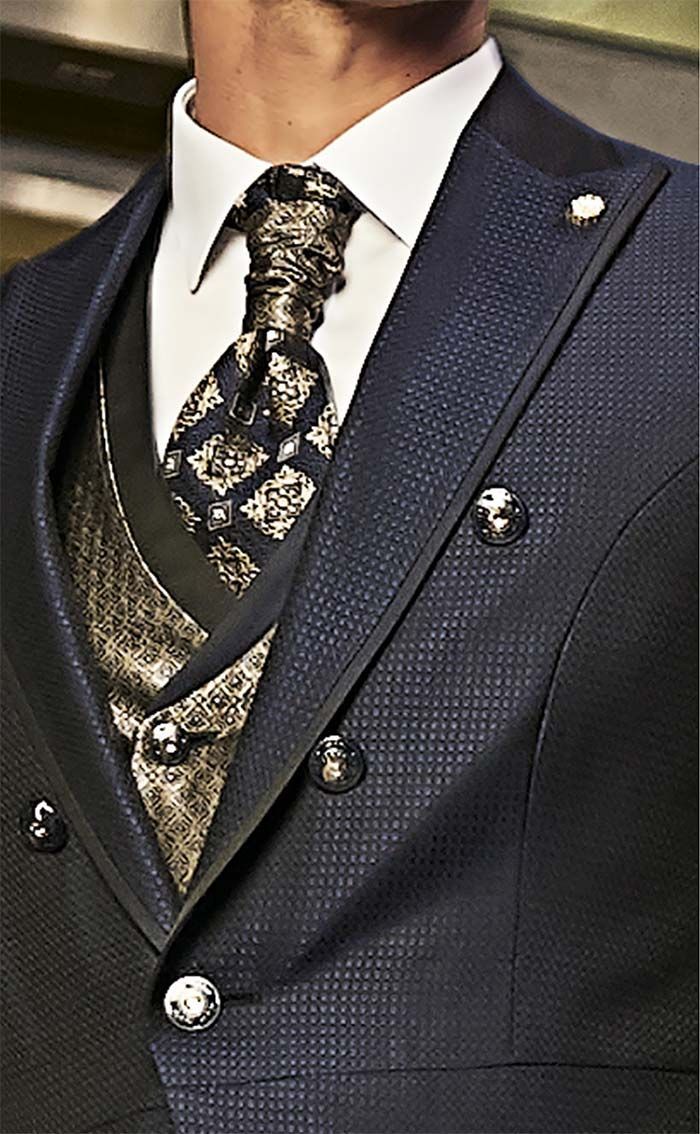 Primer pla d’un vestit blau marí de ratlles fines, amb corbata estampada i armilla de color beix