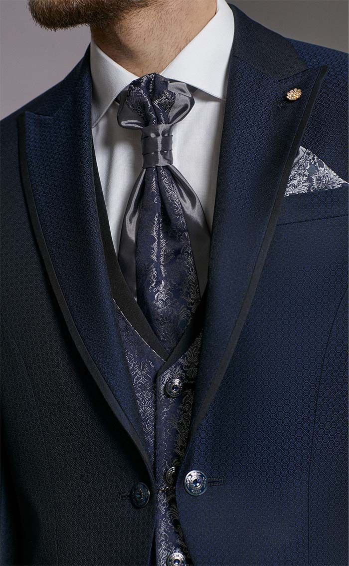 Primer pla d’un vestit blau marí amb corbata estampada, armilla i mocador de butxaca sobre una camisa de vestir