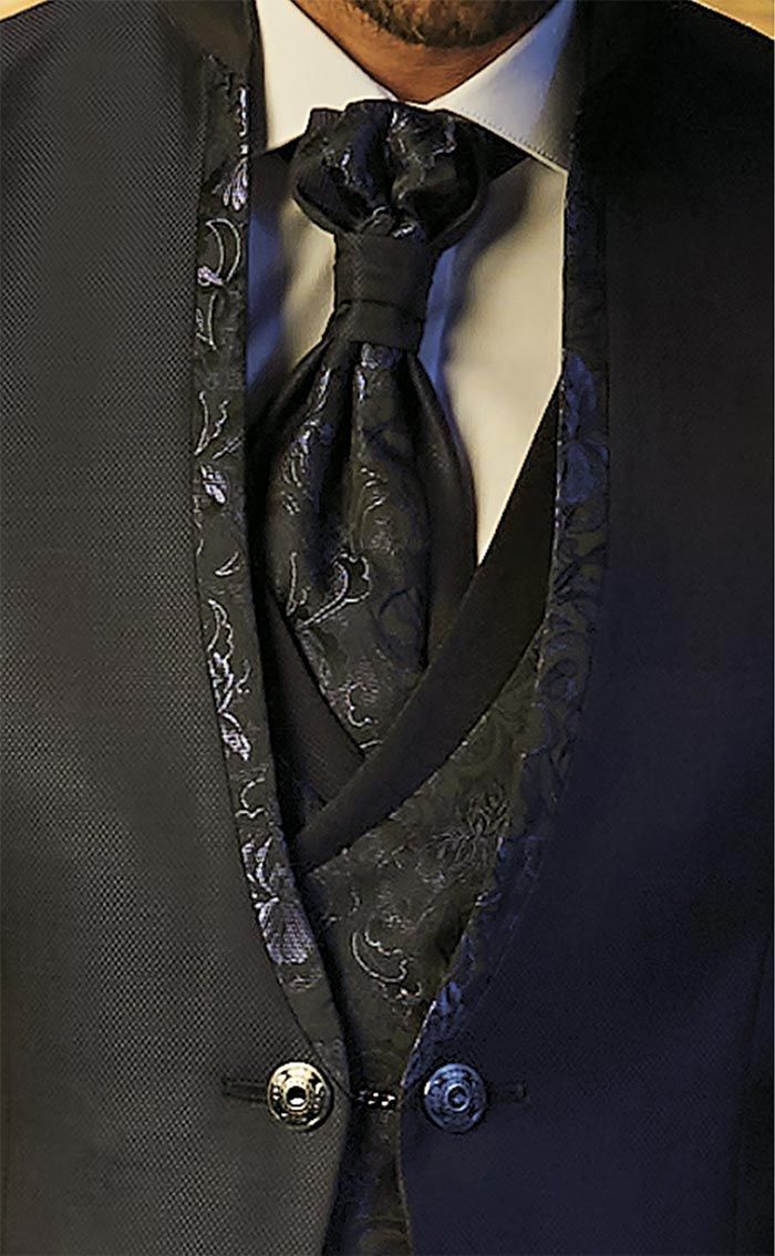 Primer pla d’una jaqueta d’esmòquing negra amb solapa de setí, armilla estampada i corbata negra.