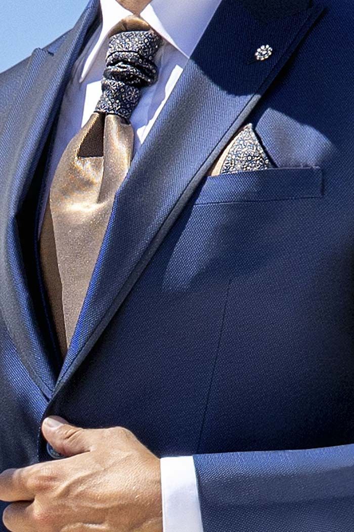 Primer pla d’un home amb vestit blau que s’arregla la jaqueta i la corbata estampada, amb un mocador de butxaca visible.