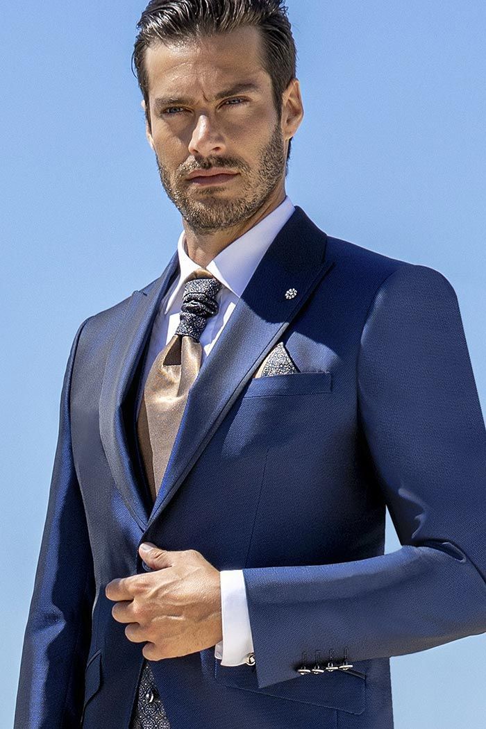 Home amb vestit blau marí i corbata, dret amb el cel blau i clar de fons, ajustant-se l’americana.