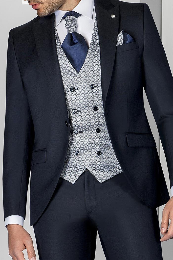 Home amb vestit blau marí, armilla platejada estampada, corbata blava i mocador de butxaca