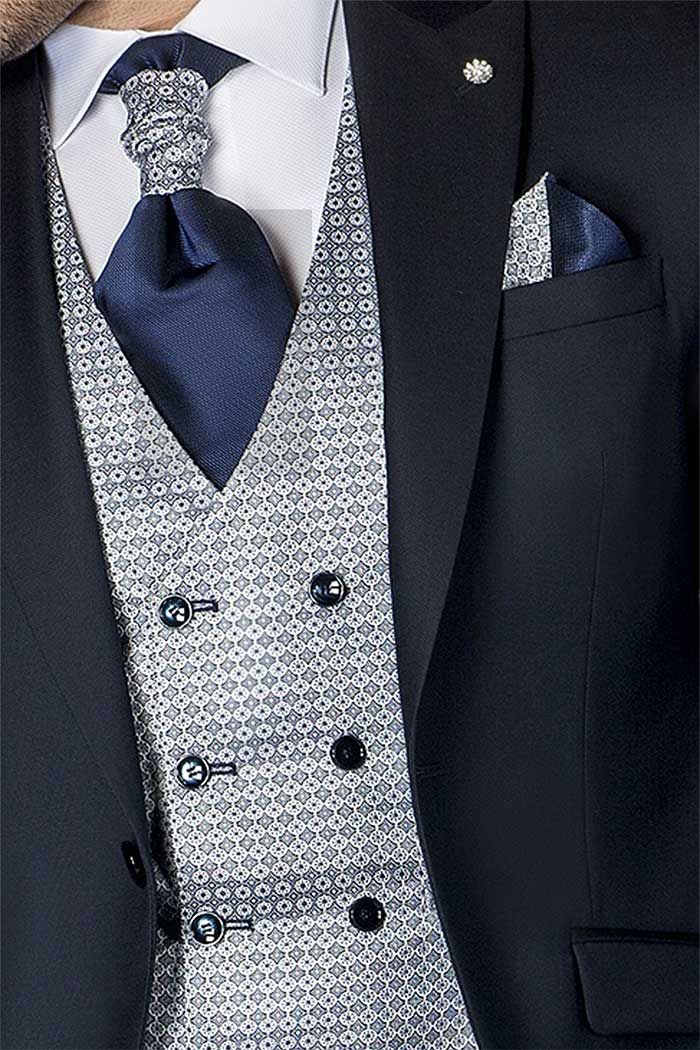 Primer pla d’un vestit blau marí amb armilla estampada, corbata i mocador de butxaca.