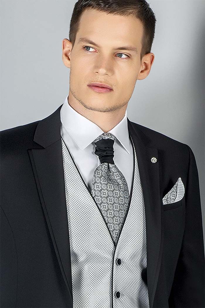 Home amb vestit negre, armilla estampada, corbata i mocador de butxaca, mirant de costat