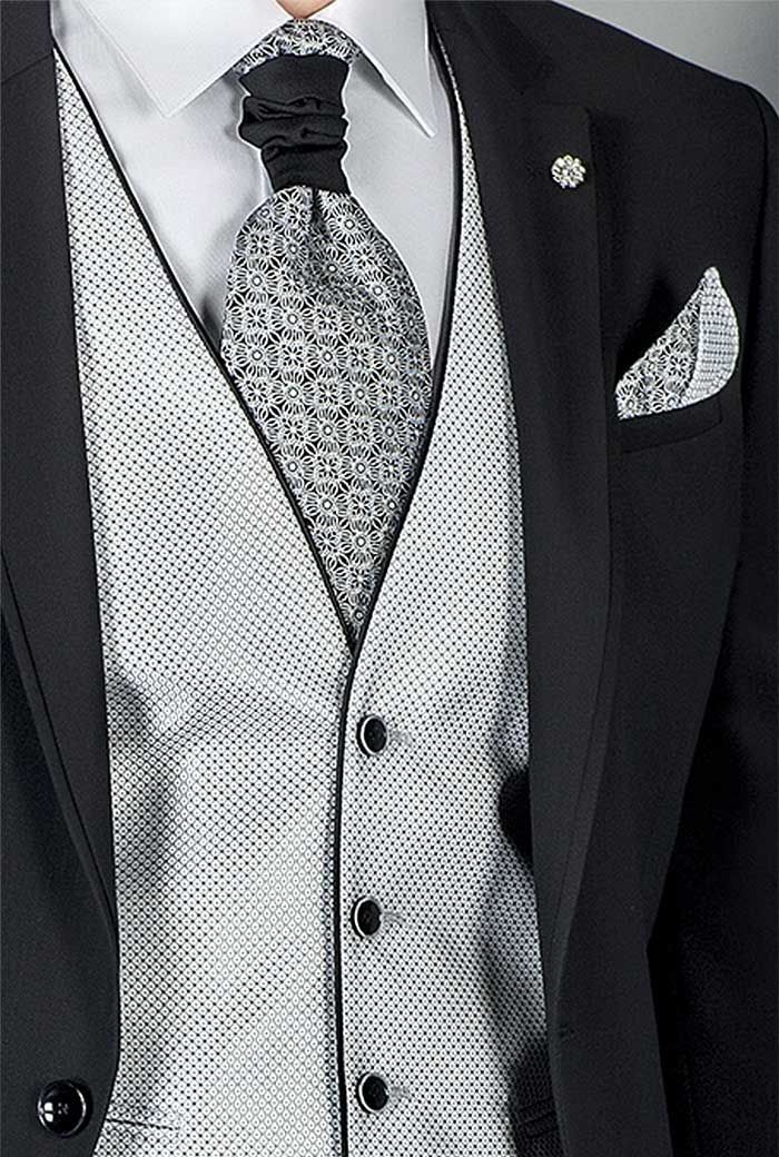 Home amb vestit negre, armilla platejada estampada, corbata negra i mocador blanc a la butxaca.