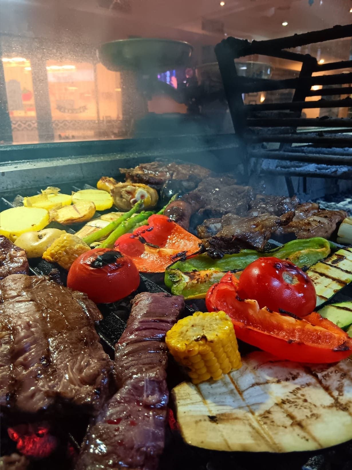 Un montón de carne y verduras se están cocinando en una parrilla.