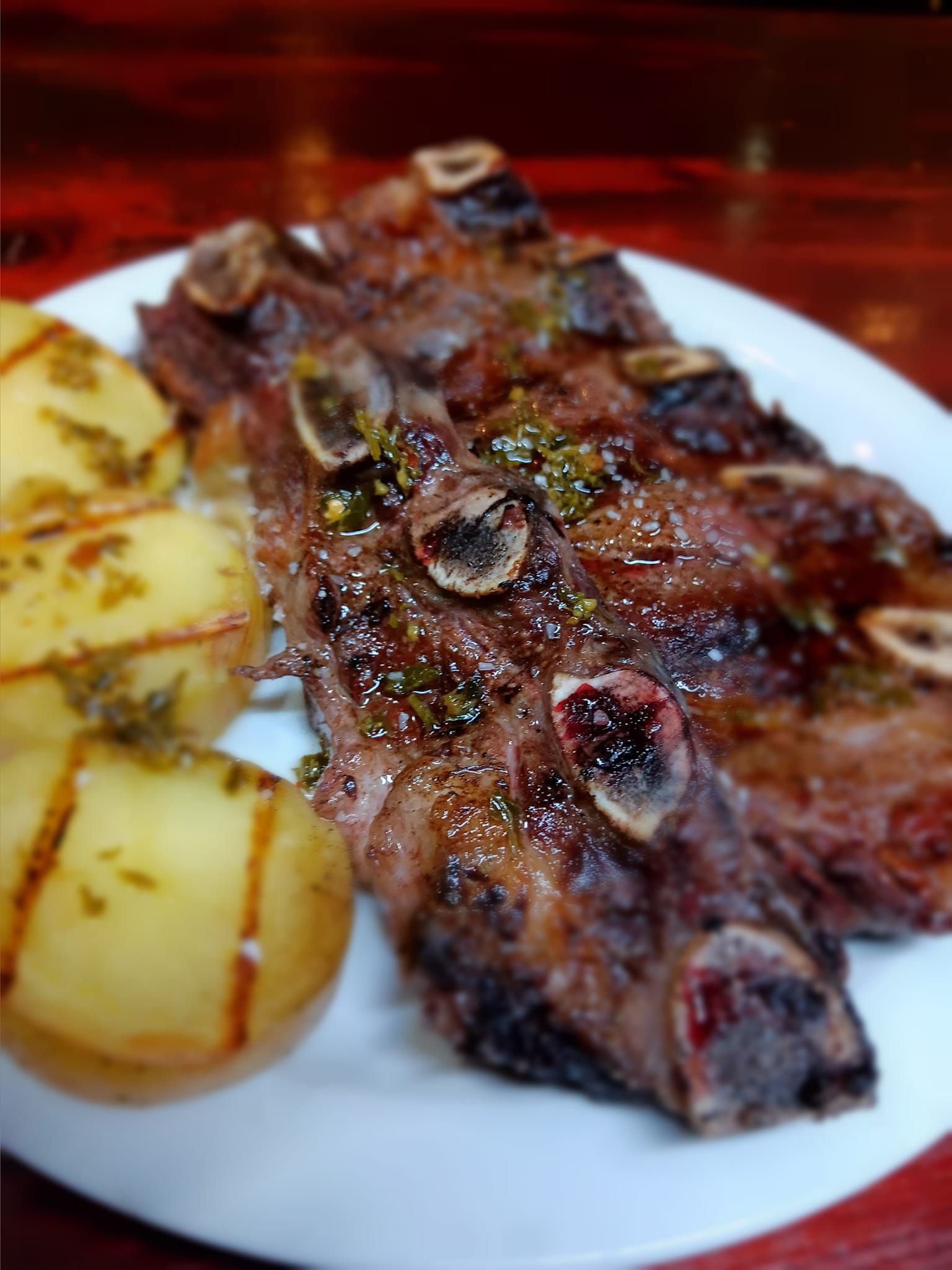 Un plato blanco cubierto con carne y patatas sobre una mesa de madera.