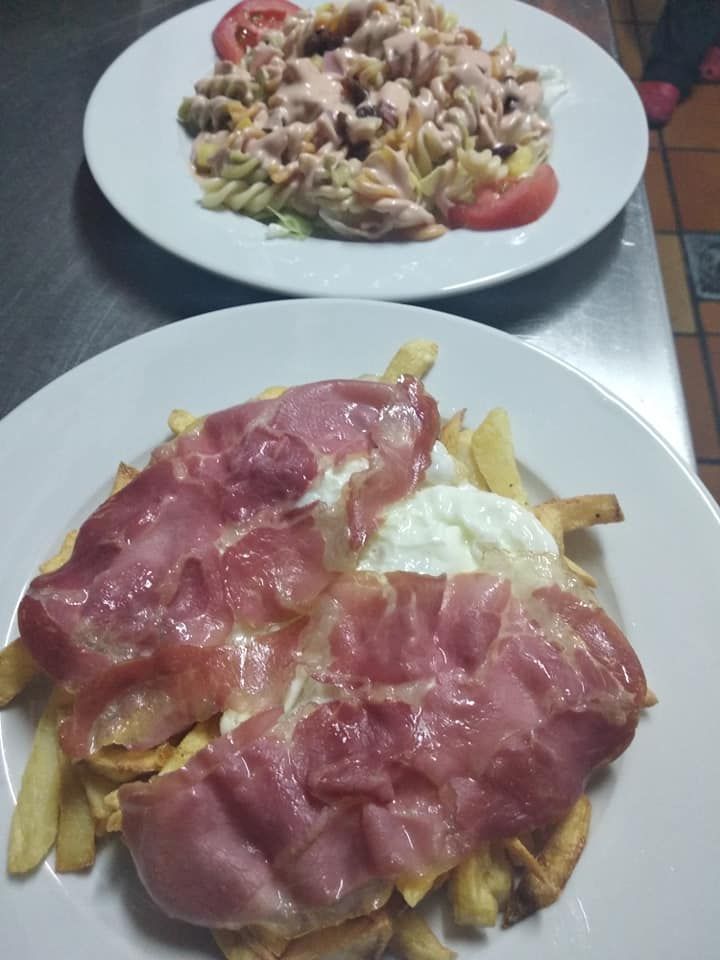 Dos platos de comida en una mesa, incluido un plato de pasta y un plato de papas fritas.