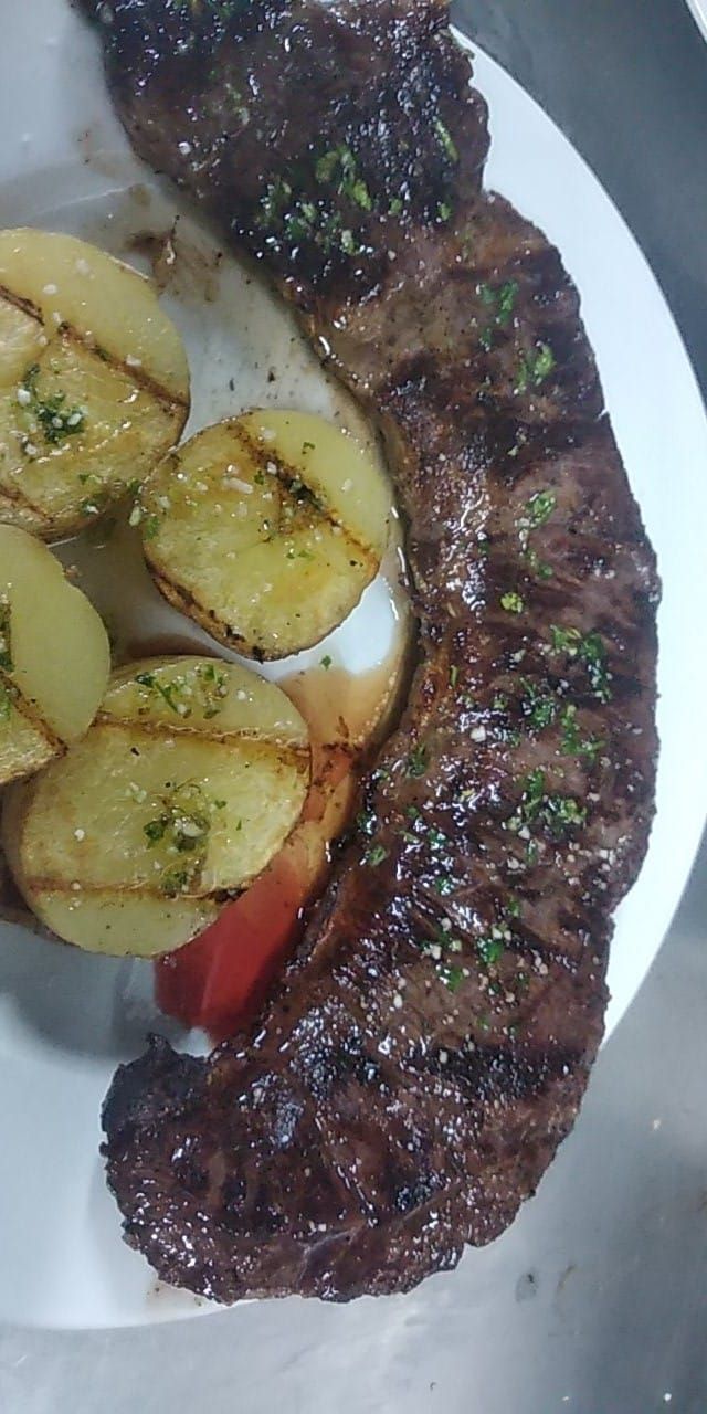 Un plato blanco cubierto con un filete y patatas.