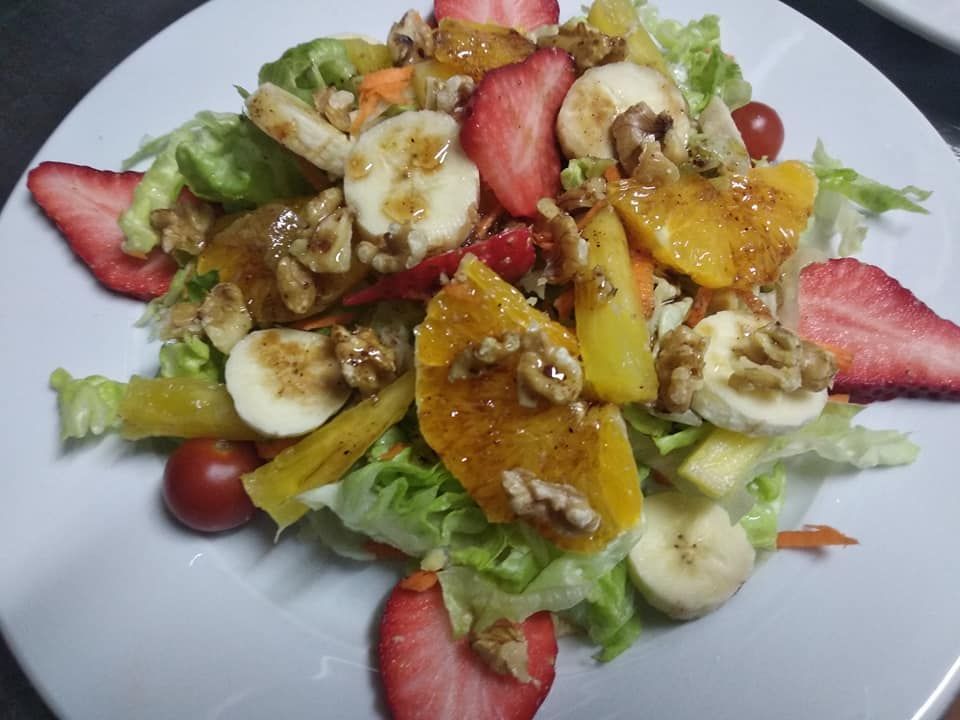 Una ensalada con plátanos, fresas y nueces en un plato blanco.