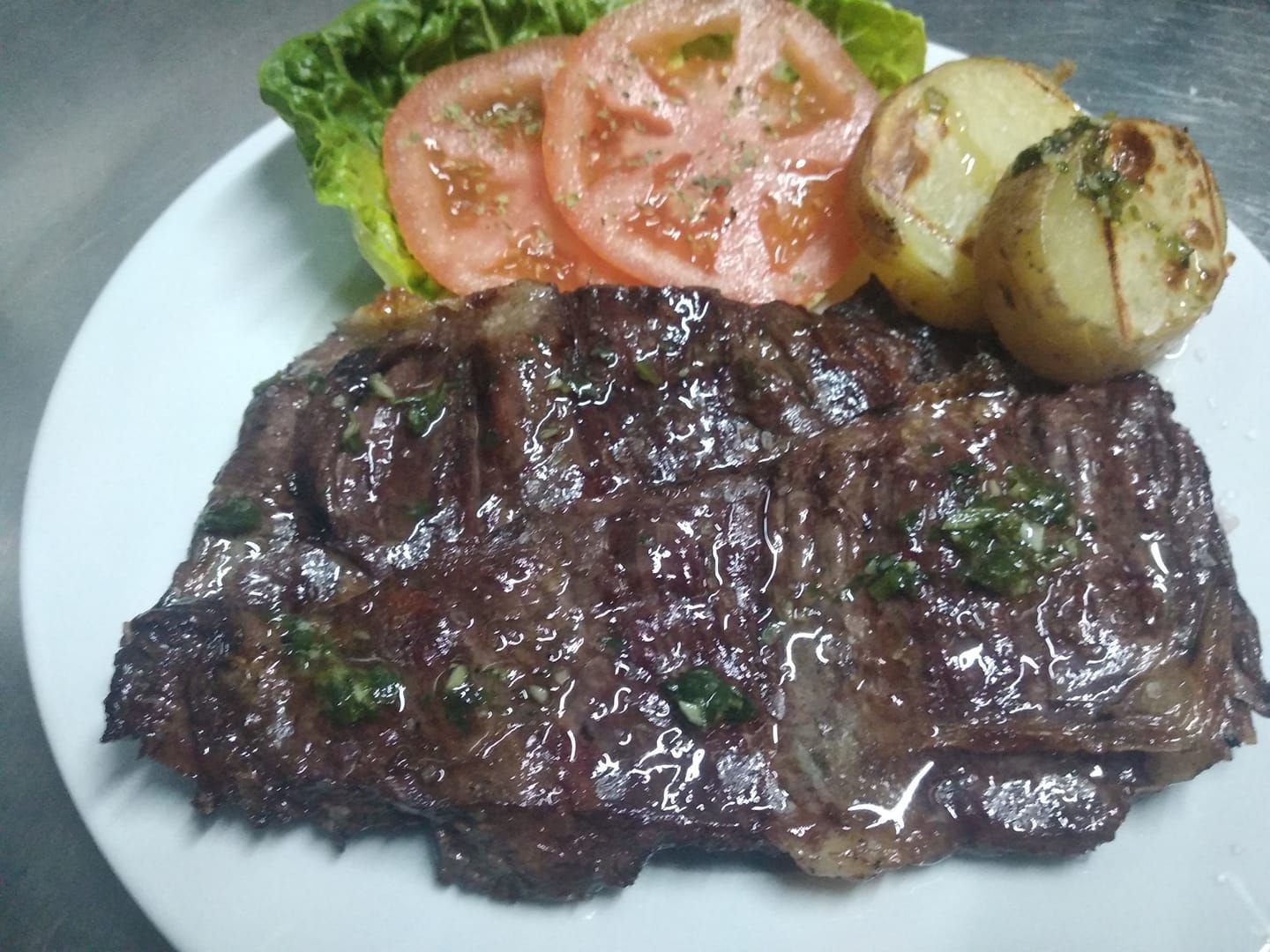 Un plato blanco cubierto con un filete, tomates y patatas.