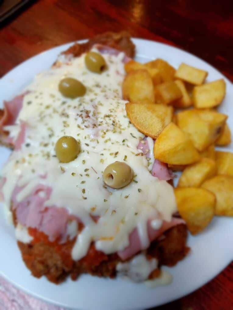 Un plato blanco cubierto con carne, queso, aceitunas y patatas.