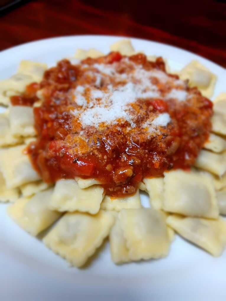 Un plato blanco cubierto con ravioles y salsa sobre una mesa.