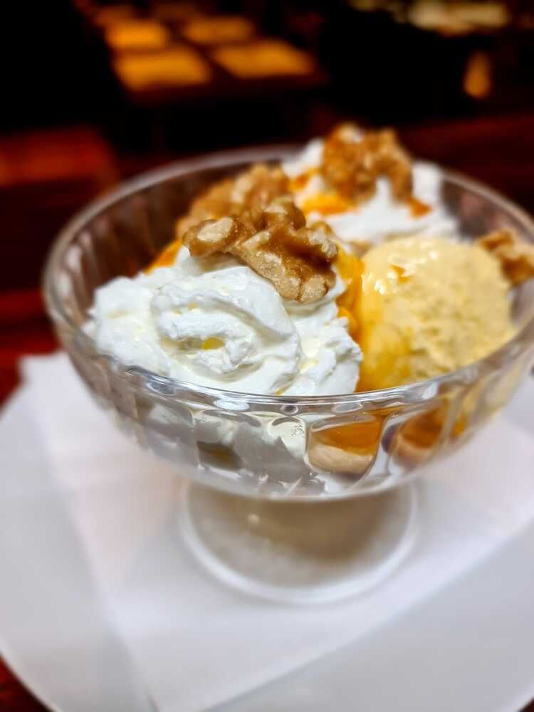 Un recipiente de vidrio lleno de helado, crema batida y nueces.