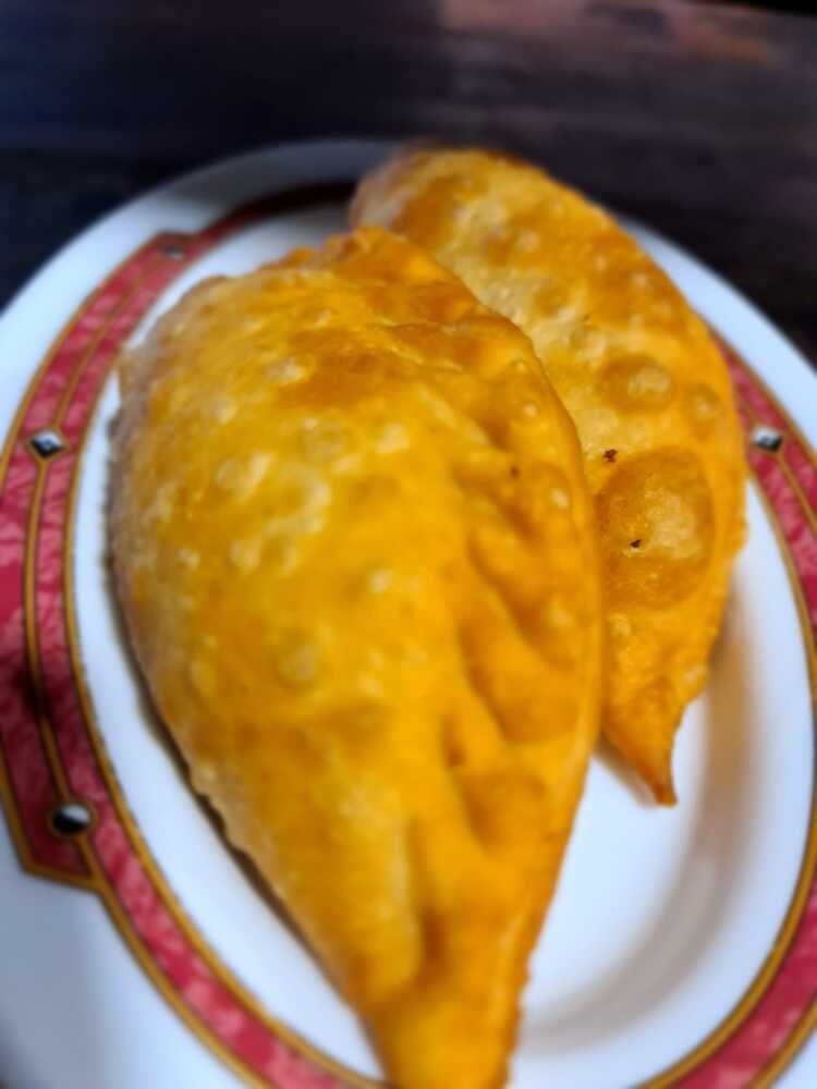 Dos pasteles fritos están en un plato blanco con un borde rojo.