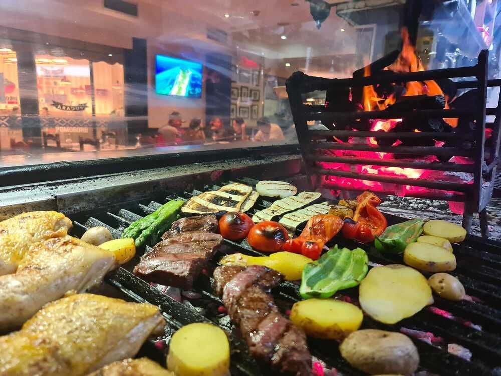 Una parrilla llena de carne y verduras con un fuego de fondo