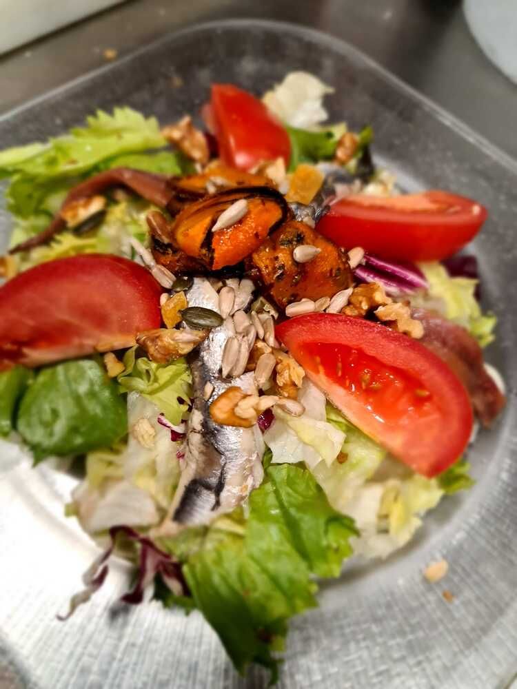 Un primer plano de una ensalada con tomates, lechuga y nueces en un plato.
