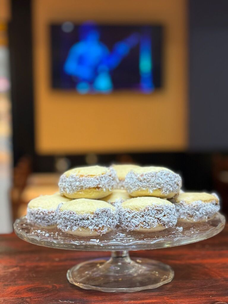 Un soporte de cristal para tartas lleno de galletas y un televisor al fondo.
