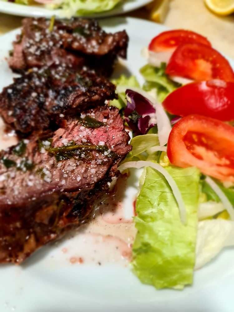 Un plato blanco cubierto con carne y verduras, incluidos tomates y lechuga.