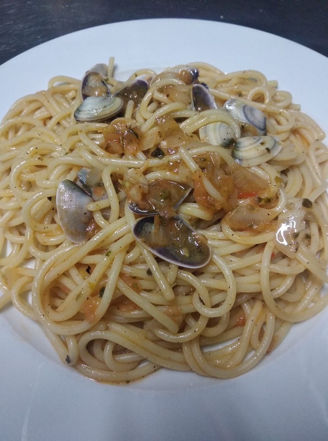 Un plato blanco cubierto con espaguetis y almejas sobre una mesa.