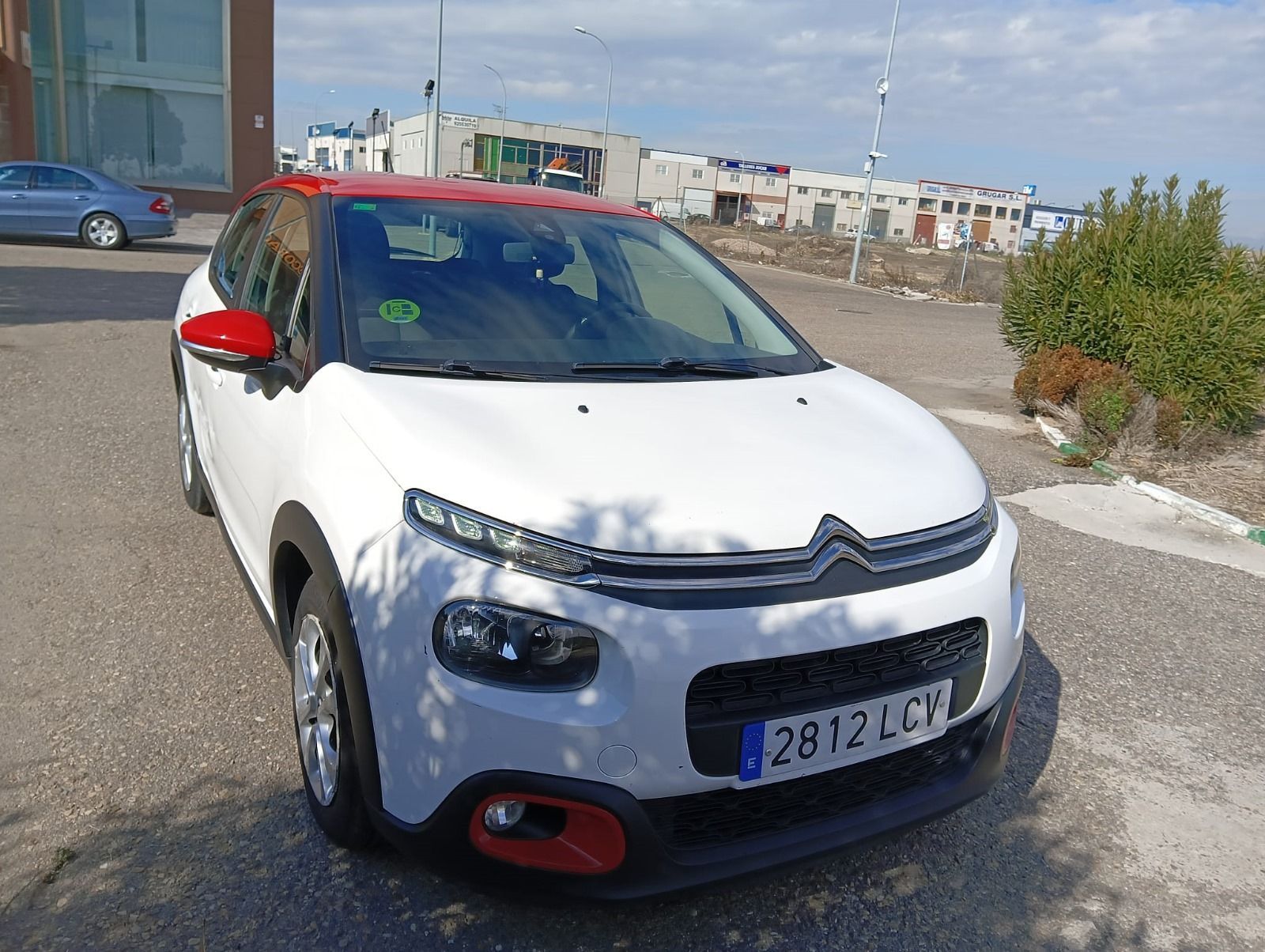 Un coche blanco con capota roja está aparcado en un estacionamiento