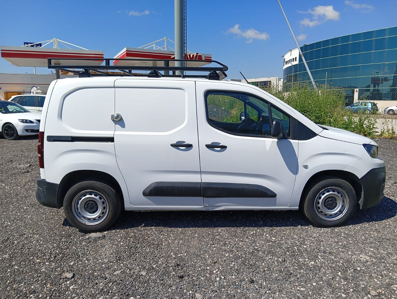 Una camioneta blanca con portaequipajes está estacionada en un estacionamiento de grava.