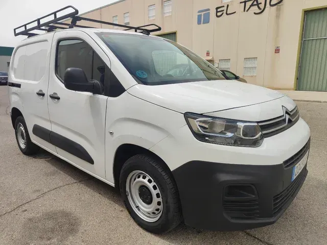 Una furgoneta blanca con portaequipajes en el techo está estacionada delante de un edificio.