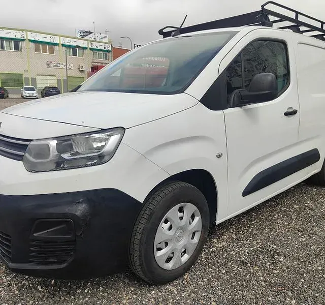 Una camioneta blanca con portaequipajes está estacionada en un estacionamiento de grava.