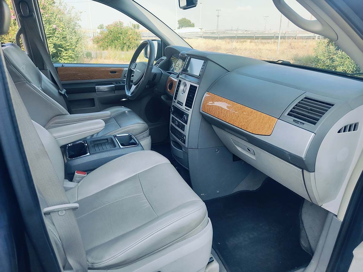 Vista interior de una minivan Chrysler con asientos de cuero gris claro, molduras de madera y tablero negro.