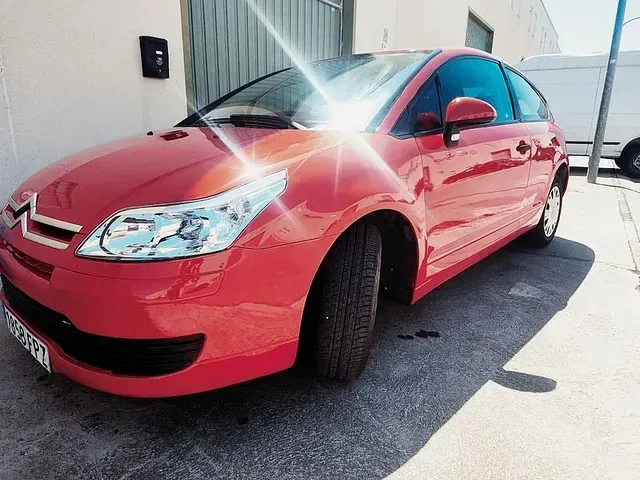 Un coche rojo está aparcado delante de un edificio.