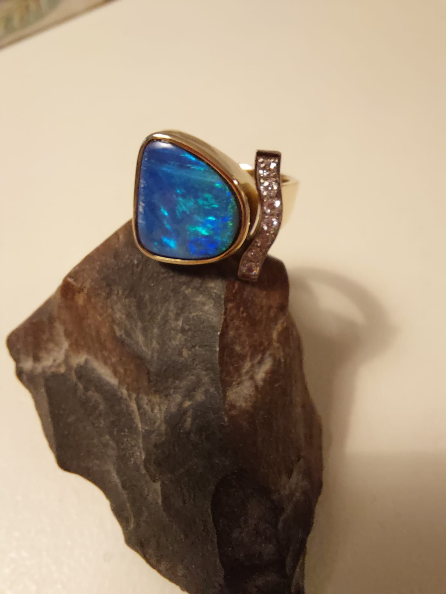 Goldring mit blauem Opal und Diamantakzent, präsentiert auf einem dunklen, rauen Stein.