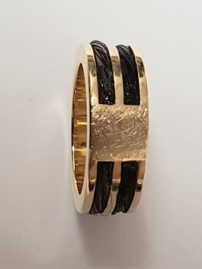 Goldring mit schwarzem Kabeldesign auf weißer Oberfläche.