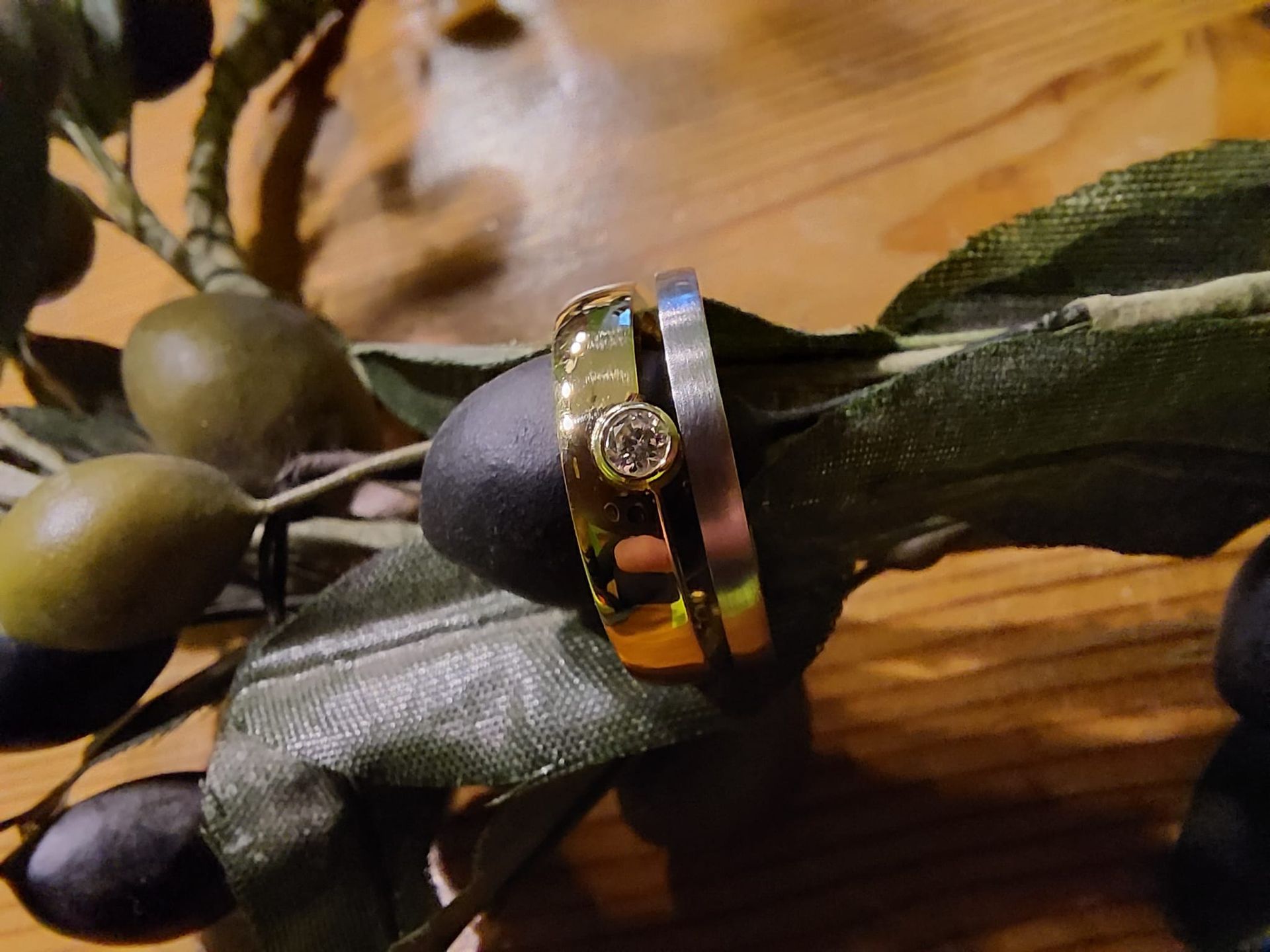 Zwei Ringe mit einem Edelstein sitzen auf einem Olivenzweig mit grünen und schwarzen Oliven.
