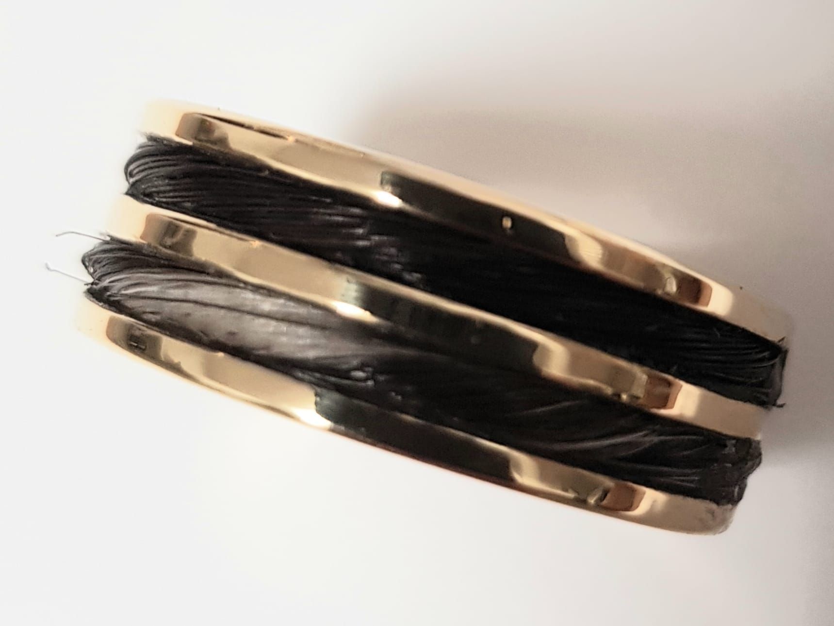 Goldener Armreif mit schwarzen Strängen zwischen goldenen Bändern.