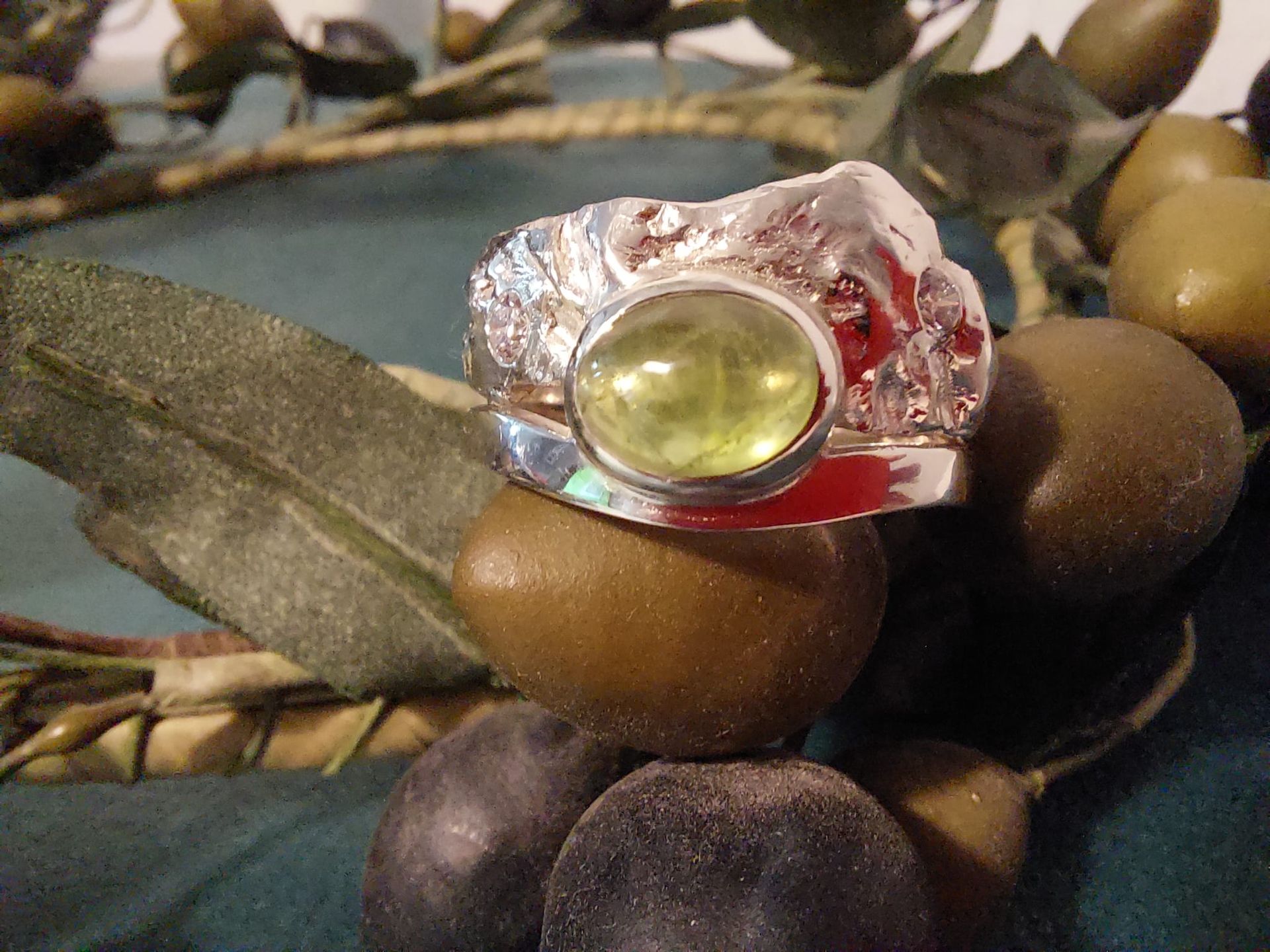 Silberring mit großem ovalen grünen Edelstein, auf braunen Oliven.