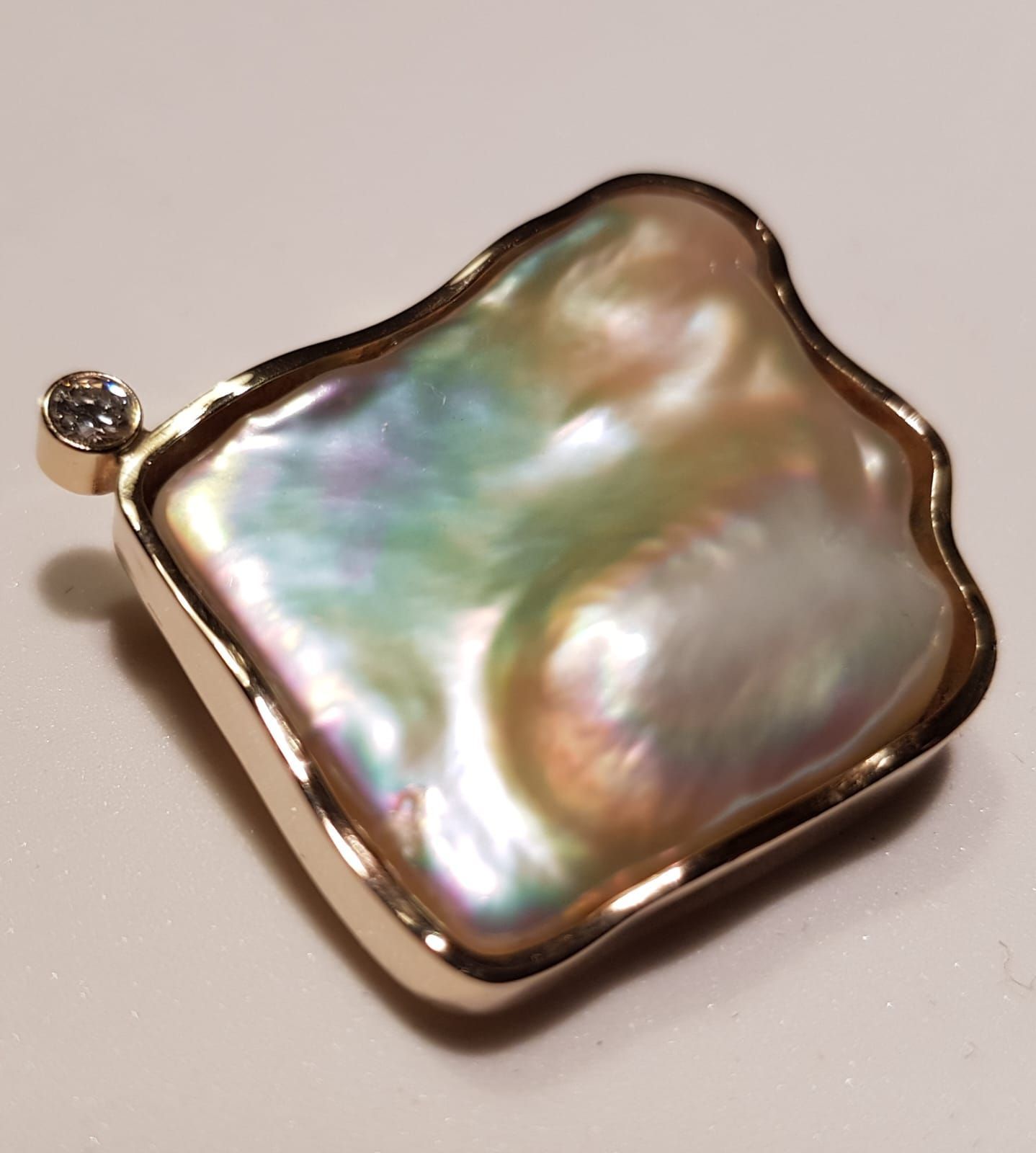 Goldanhänger mit einer großen, unregelmäßig geformten, schillernden Perle und einem kleinen Diamanten.