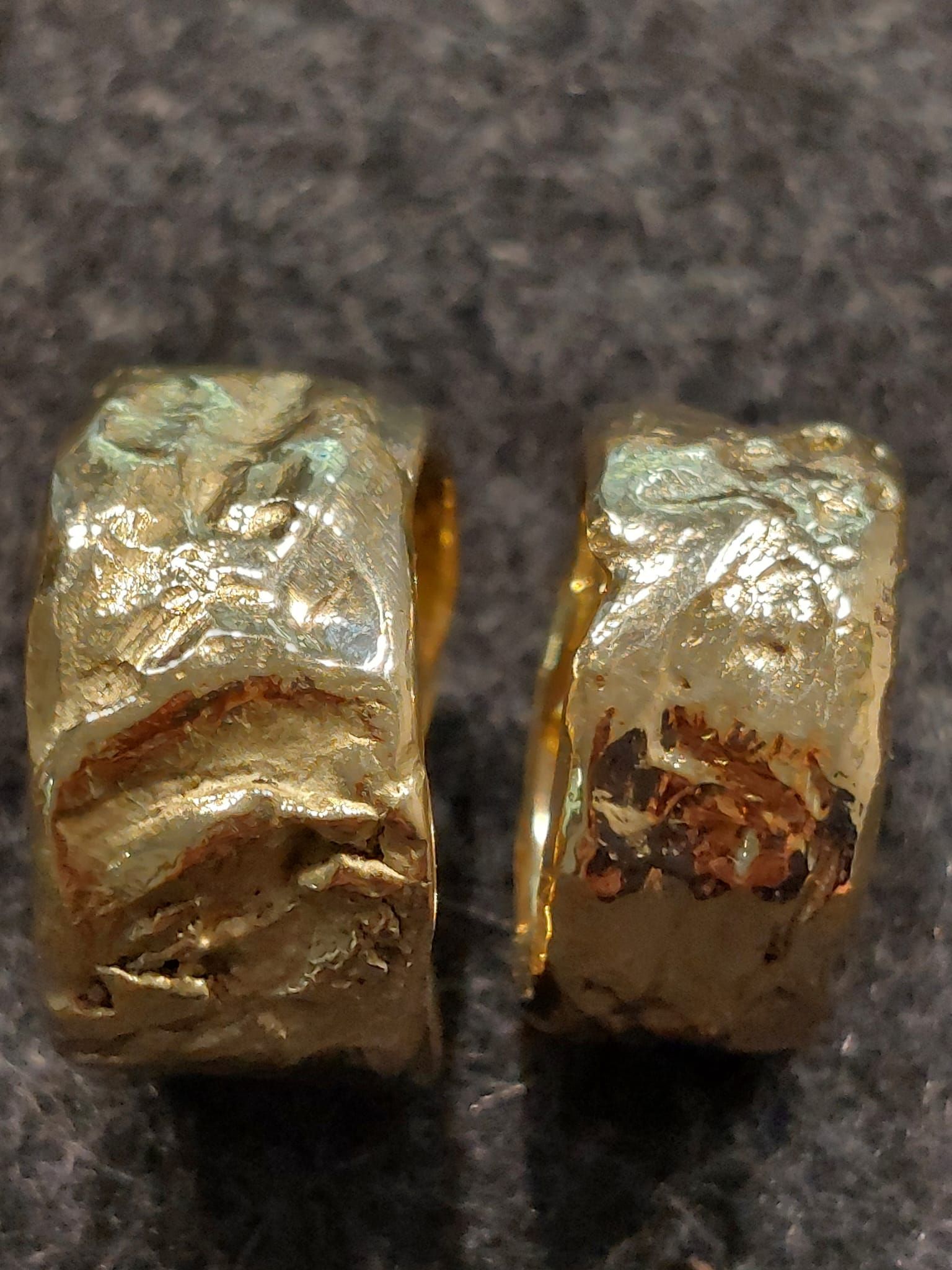 Zwei strukturierte goldene Creolen auf einer dunklen Oberfläche.