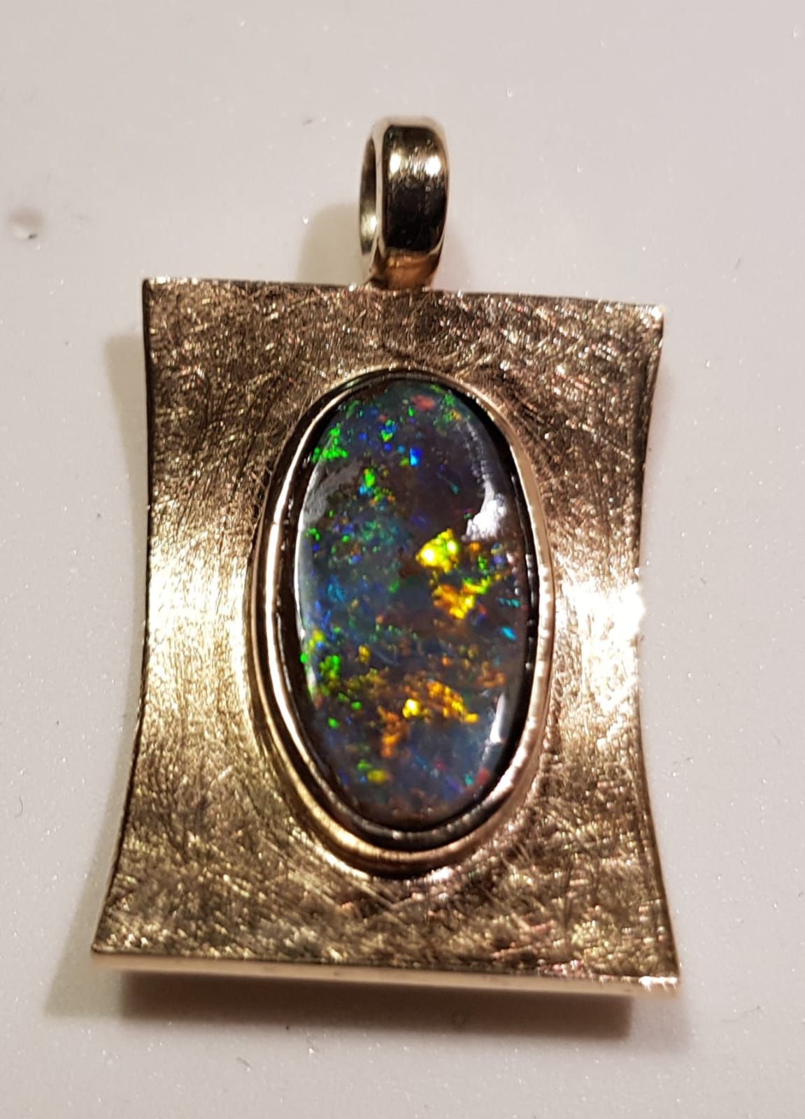 Goldanhänger mit einem ovalen schwarzen Opal mit einem Farbspiel aus Grün, Blau und Orange.