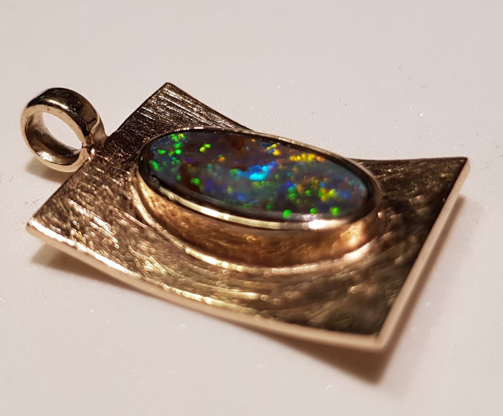 Goldanhänger mit schwarzem Opal-Edelstein, der bunte Lichtblitze zeigt, eingefasst in eine ovale Fassung.