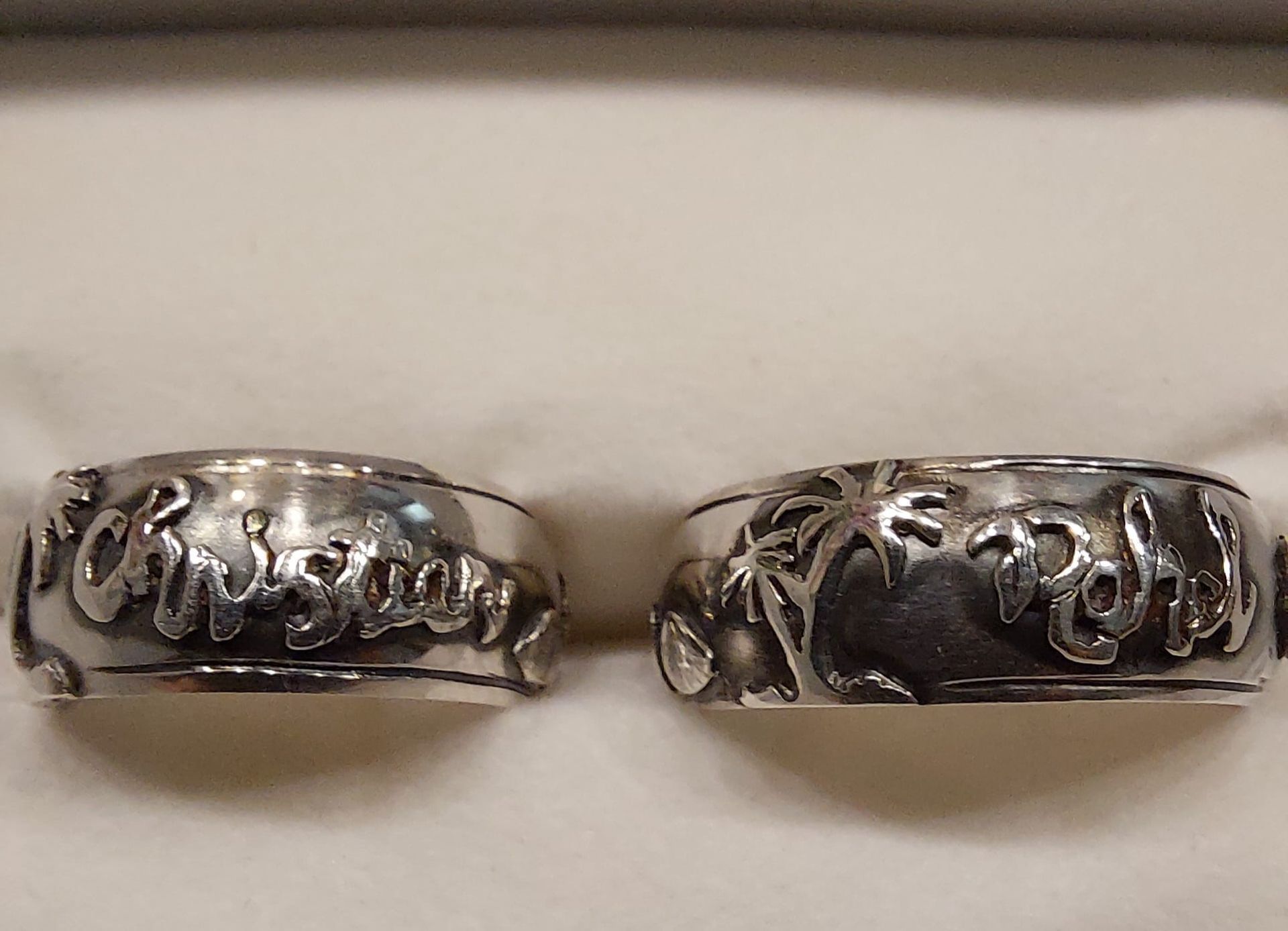 Zwei silberne Ringe mit eingraviertem Text und Mustern, Nahaufnahme.