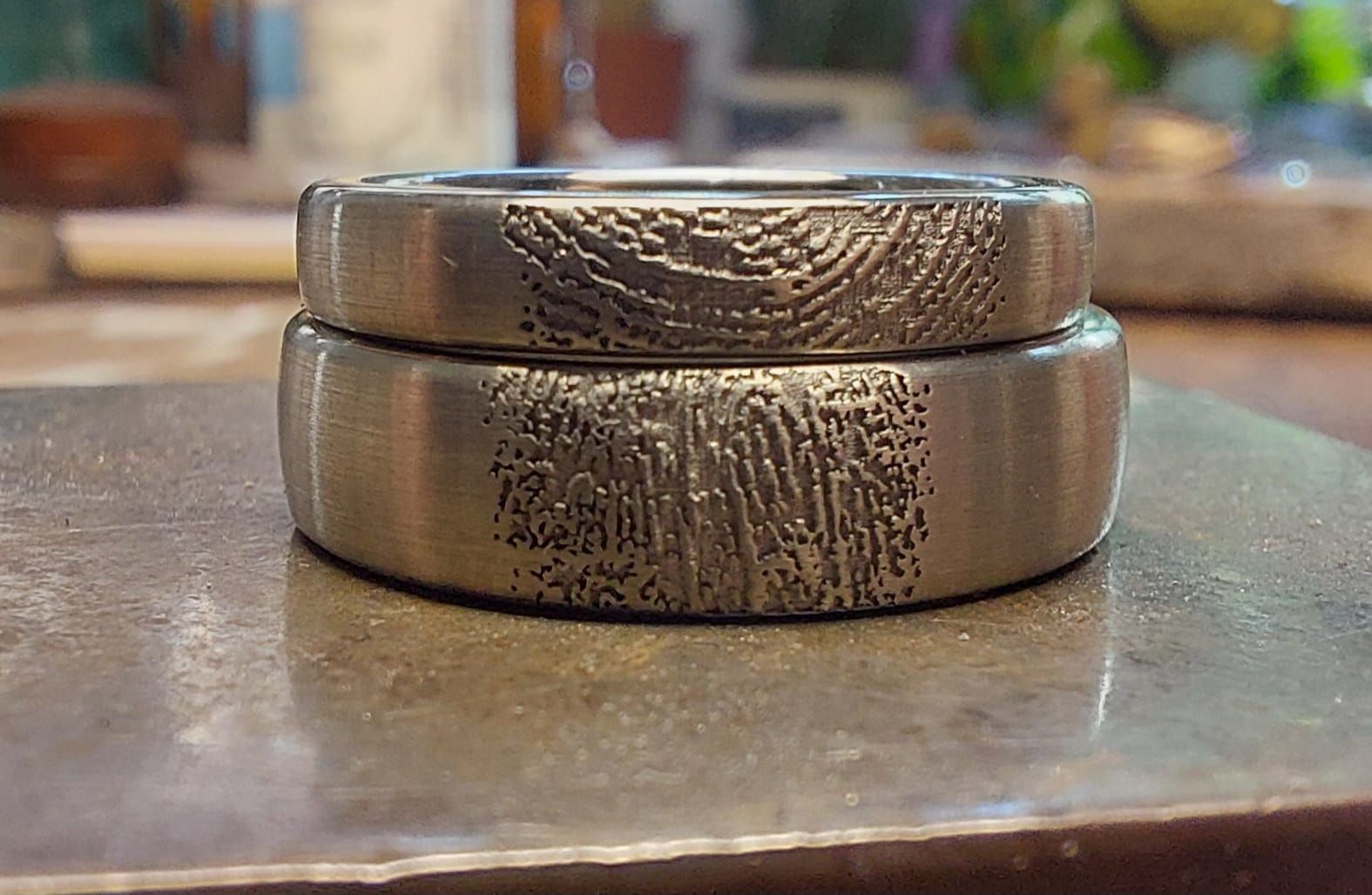 Zwei übereinander liegende Silberringe, jeder mit einem in das äußere Band eingravierten Fingerabdruck-Design.