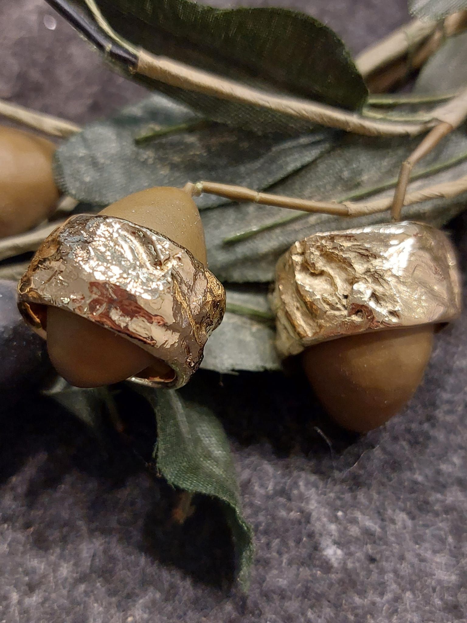 Zwei Eicheln mit goldfarbenen Kappen und grünen Blättern.