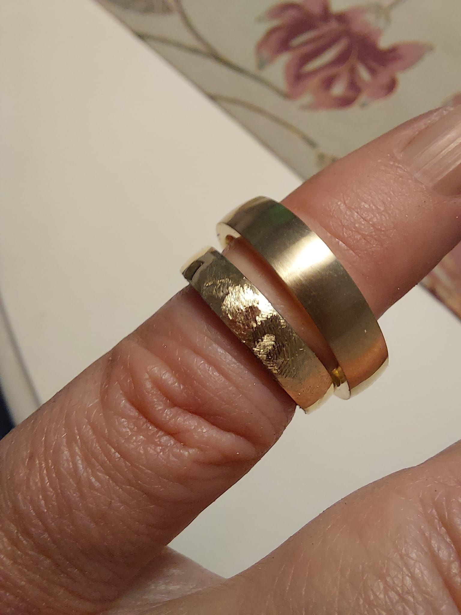 Zwei goldene Ringe an einem Finger, einer mit strukturierter Oberfläche, möglicherweise getragen.